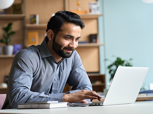 Smiling man seated at a desk using a laptop computer.