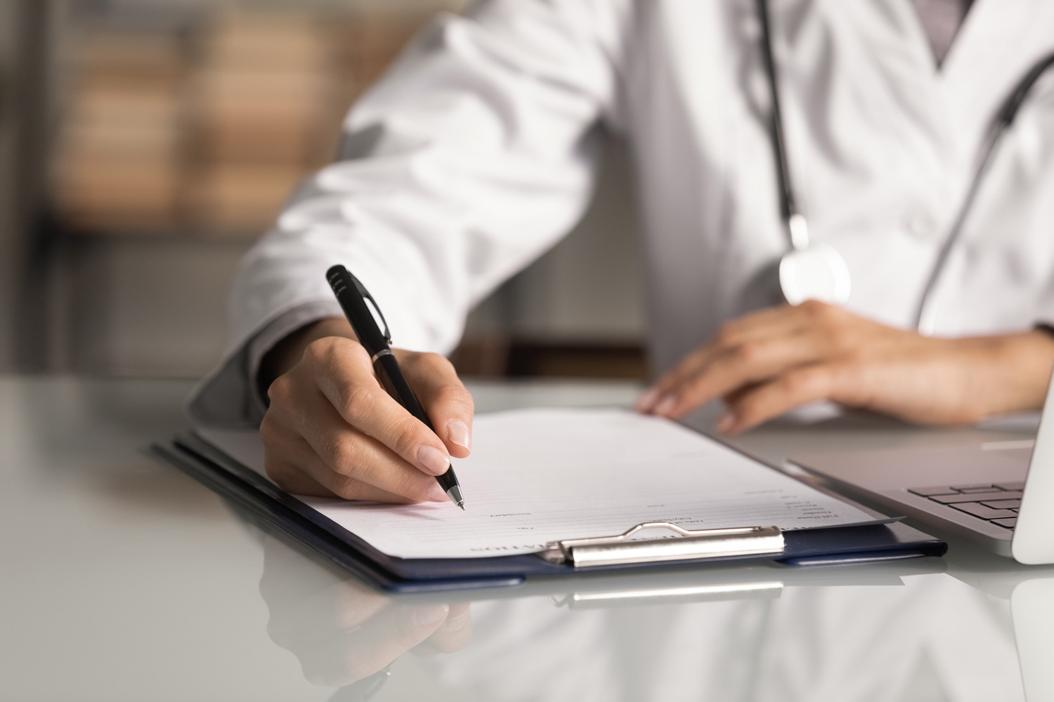 This is an image of a healthcare provider in a white lab coat with a stethoscope documenting on a clipboard.