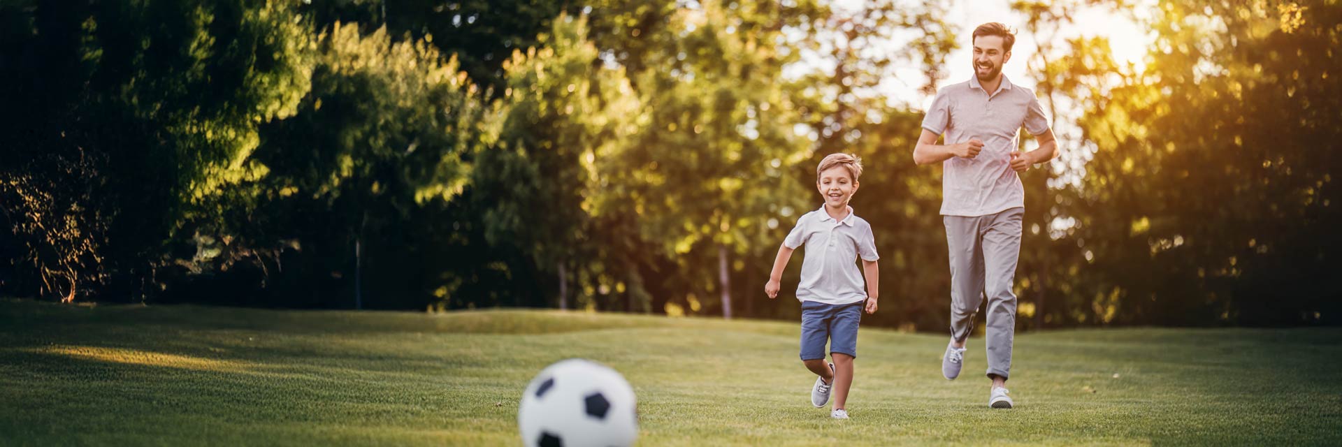 A father and young son happily playing soccer in a sunlight field